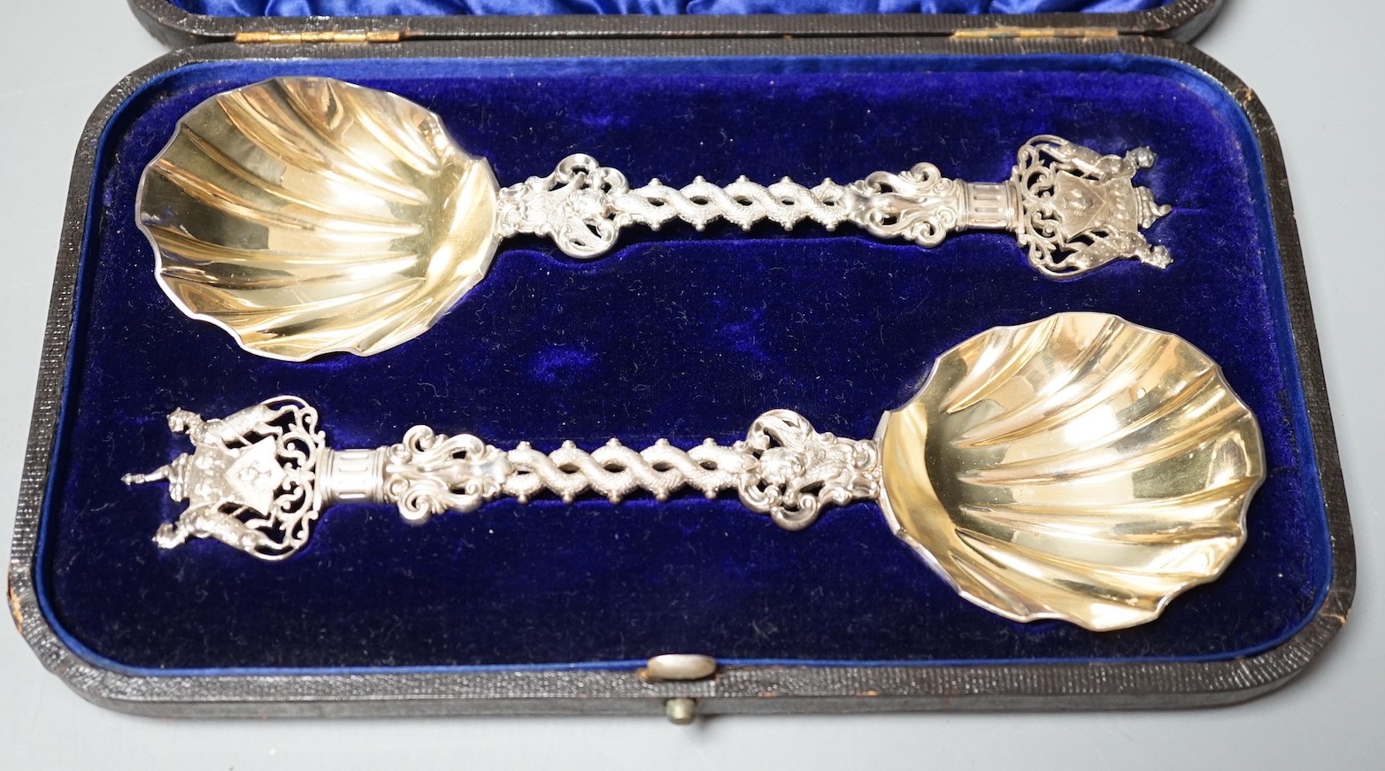 A cased pair of ornate late Victorian silver serving spoons, with entwined stems and terminals modelled as the crest of The Salter's Company, Francis Higgins III, London, 1894, 19.5cm, 5oz.